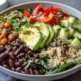 Close-up view of a hearty Three-Bean Power Bowl showing diced red bell peppers, cucumbers, and a zesty dressing drizzle.