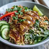 A close-up of a hearty Peanut Chicken Power Bowl shows juicy chicken, shredded purple cabbage, and fresh spinach tossed with a savory peanut dressing for a satisfying meal.