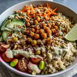 A close-up view of a Peanut Chickpea Protein Bowl topped with chopped peanuts, fresh cilantro, and lime wedges.