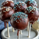 Festive graduation cake pops in vibrant school colors, each topped with a fondant cap and chocolate tassel.