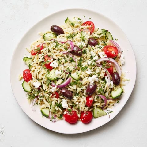 Spilled Greek Orzo Salad on a rustic wooden table, showcasing vibrant red tomatoes, green cucumber, and white feta, perfect for a summer picnic or potluck side dish.