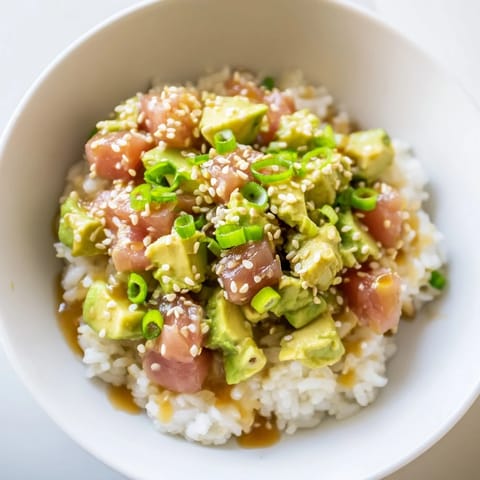 Close-up of a Tuna Avocado Rice Bowl drizzled with sesame-soy dressing, featuring fresh cilantro and nori strips for garnish.