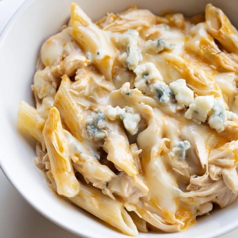 Creamy Buffalo Chicken Pasta in a white bowl, garnished with crumbled blue cheese and fresh chives, steam rising.