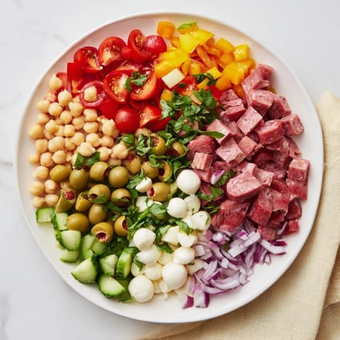 A close-up of Crunchy Antipasto Chopped Salad with salami, mozzarella pearls, and colorful veggies in a zesty Italian dressing.