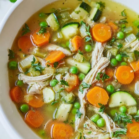 Vibrant bowl of Spring Garden Chicken Soup with tender shredded chicken, fresh peas, and crisp carrots in a savory herb broth.  