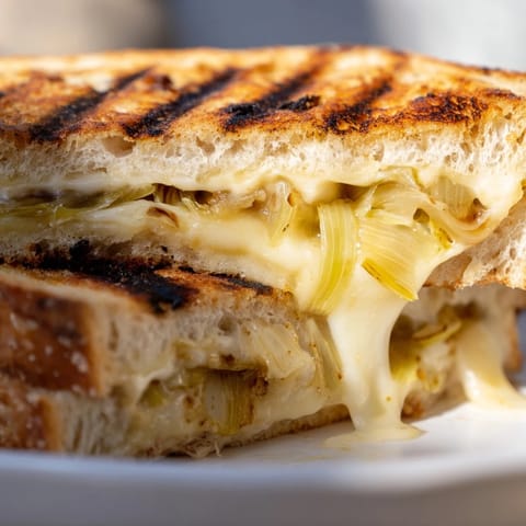 A close-up of Havarti & Caramelized Leek Grilled Cheese highlights melting cheese and sweet leeks on crisped, golden-brown bread.