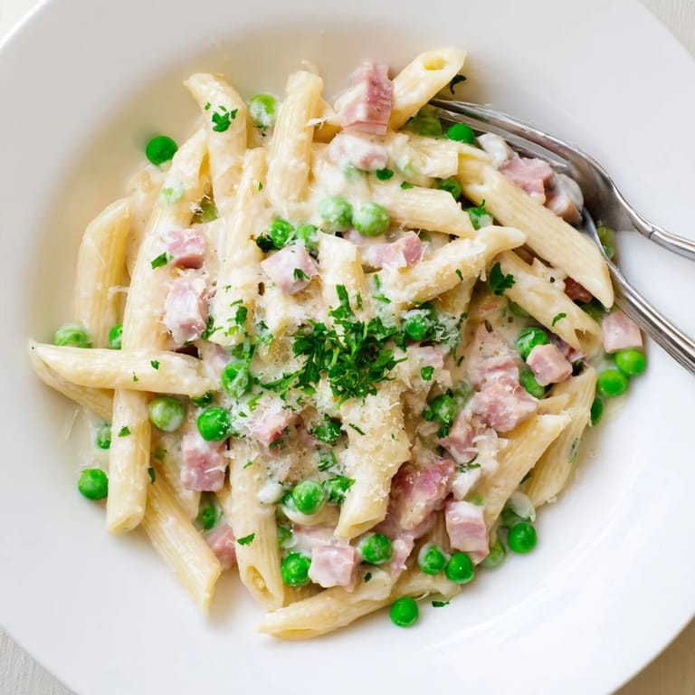 Steaming bowl of Spring Pea & Ham Pasta served with a glass of chilled white wine on a rustic table.  