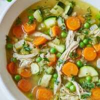 Vibrant bowl of Spring Garden Chicken Soup with tender shredded chicken, fresh peas, and crisp carrots in a savory herb broth.  
