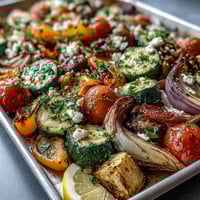 Freshly roasted Mediterranean Greek vegetables with eggplant, zucchini, and peppers topped with crumbled feta and parsley on a white plate.