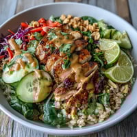 Sliced baked chicken and crisp veggies sit atop fluffy brown rice in a vibrant Peanut Chicken Power Bowl, drizzled with creamy peanut sauce and garnished with chopped peanuts.